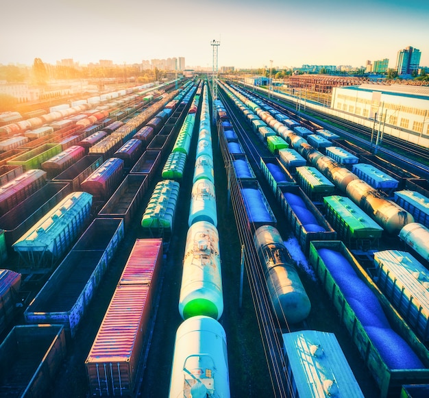 Vista aérea de coloridos trenes de mercancías al atardecer. Vagones de carga con mercancías en la estación de tren. Ferrocarril. Industria pesada. Paisaje industrial con andén ferroviario. Vista superior del zumbido del depósito. Urbano