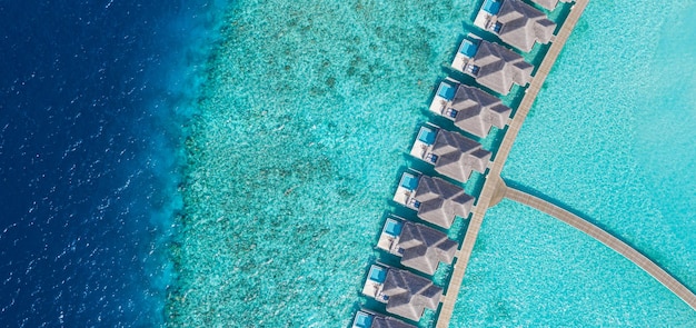 Vista aérea del complejo de villas de agua de lujo de la isla de Maldivas y el muelle de madera Hermoso cielo y océano