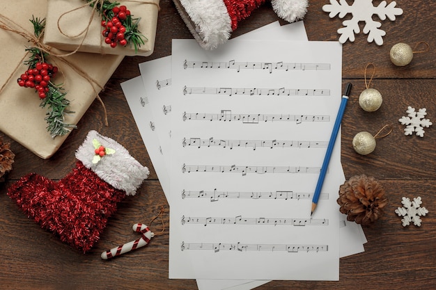 Vista aérea del concepto del fondo de la Feliz Navidad y de la música Decoraciones y ornamento esenciales con las notas blancas de papel Objetos en el estudio rústico moderno marrón de la tabla en casa Artículos esenciales para la estación.