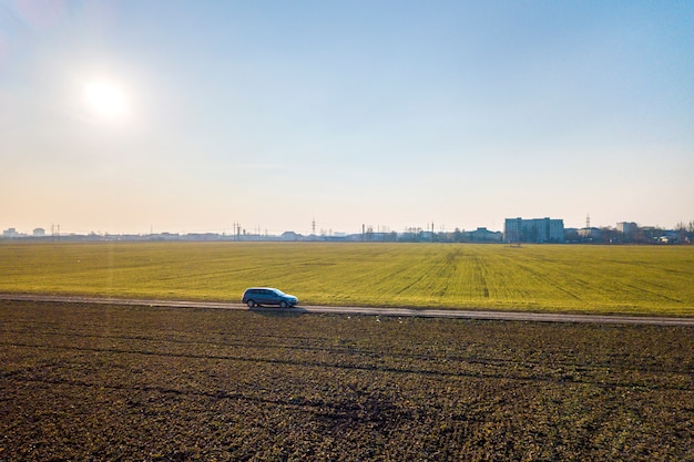 Vista aérea de la conducción de automóviles por camino de tierra recta a través de campos verdes sobre fondo de espacio soleado cielo azul copia. Fotografía de drones.