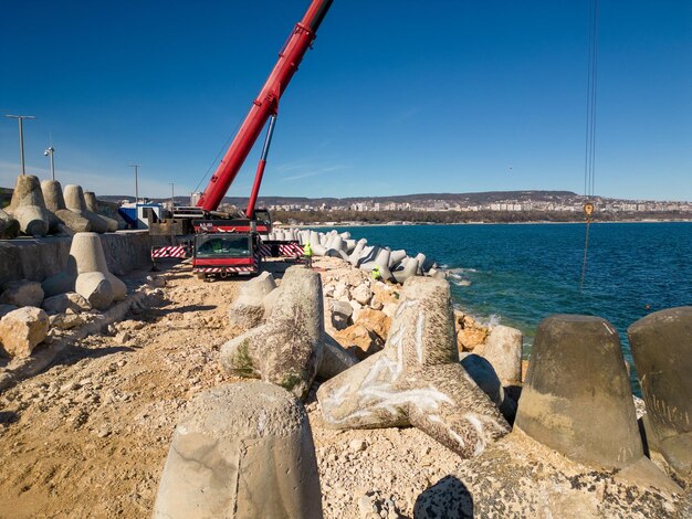 Vista aérea de la construcción del rompeolas Bulldozer y grúa sobre un montón de rocas en el mar