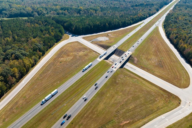 Vista aérea del cruce del paso elevado de la autopista con automóviles y camiones de tráfico rápido en la infraestructura de transporte interestatal del área rural estadounidense en EE.UU.