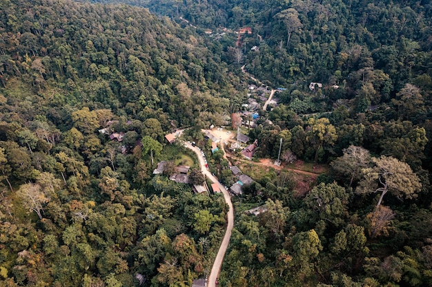 Vista aérea da aldeia rural local com estrada de cascalho no vale distante no campo entre a floresta tropical no Sudeste Asiático