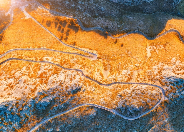 Vista aérea da estrada de montanha curva com carros, floresta laranja ao pôr do sol no outono