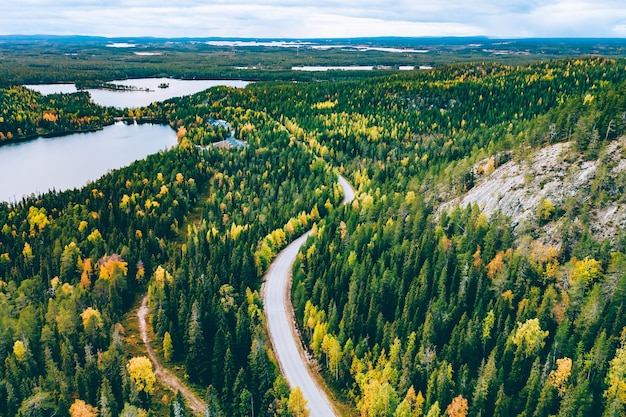 Vista aérea da estrada rural na floresta de outono amarela e laranja com lago azul na Finlândia Lapônia