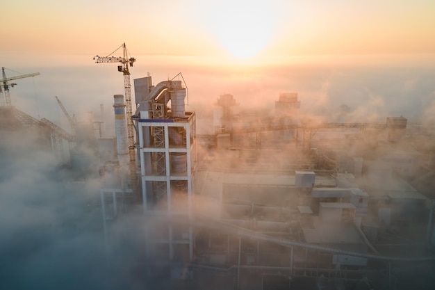 Vista aérea da fábrica de cimento com alta estrutura de planta de concreto e guindaste de torre no local de produção industrial na manhã nublada fabricação e conceito de indústria global