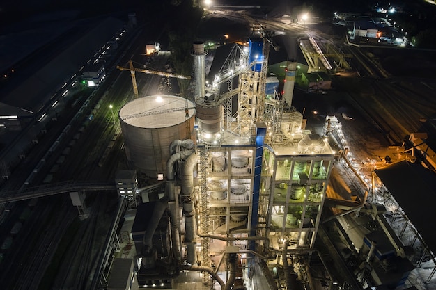 Vista aérea da fábrica de cimento com alta estrutura de planta de concreto e guindastes de torre na área de produção industrial à noite. Conceito de fabricação e indústria global.