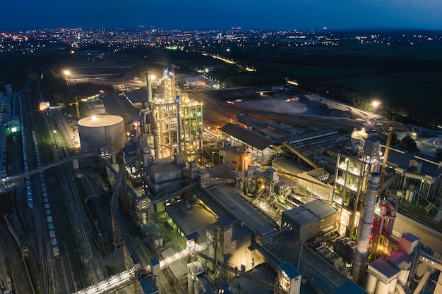 Vista aérea da fábrica de cimento com alta estrutura de planta de concreto e guindastes de torre na área de produção industrial à noite. conceito de fabricação e indústria global.