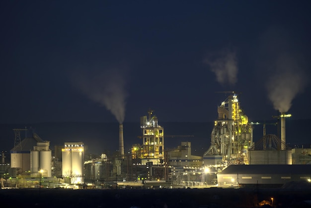 Vista aérea da fábrica de cimento com alta estrutura de planta de concreto e guindastes de torre na área de produção industrial à noite Fabricação e conceito de indústria global