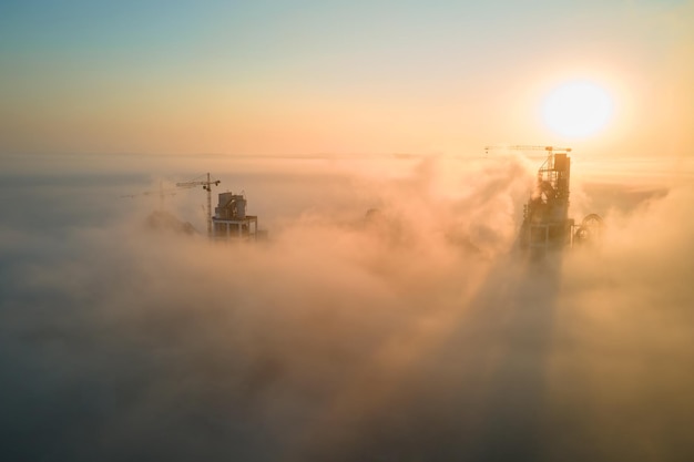 Vista aérea da fábrica de cimento com estrutura de planta alta de concreto e guindaste de torre no local de fabricação industrial na noite de nevoeiro. Produção e conceito de indústria global.
