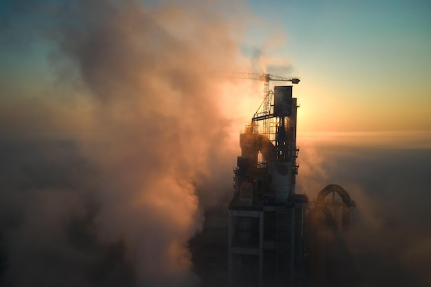 Vista aérea da fábrica de cimento com estrutura de planta de concreto alto e guindaste de torre no local de fabricação industrial na noite de neblina produção e conceito de indústria global