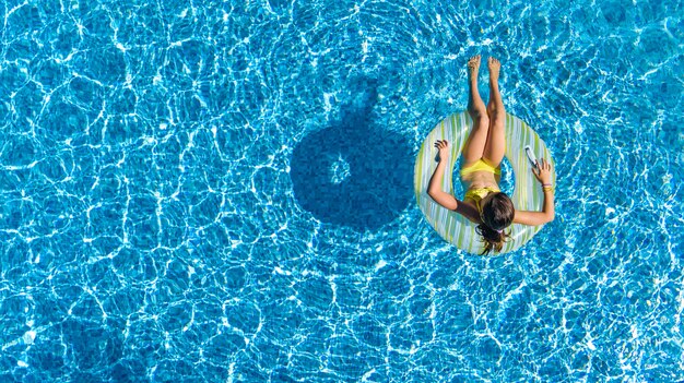 Vista aérea da garota na piscina de cima, garoto nadar na rosquinha de anel inflável e se diverte na água em férias em família