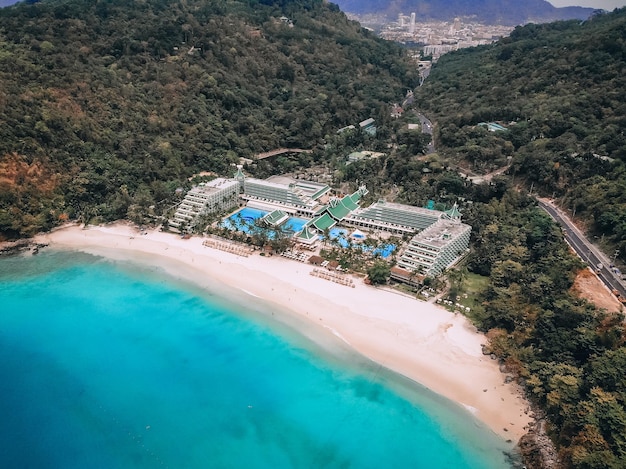 Vista aérea da idílica baía com praia arenosa e luxuoso hotel entre as colinas arborizadas; conceito de paraíso.