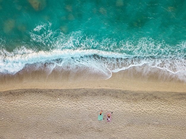 Vista aérea da incrível praia idílica com duas pessoas solitárias perto do mar acenado.