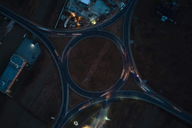 Vista aérea da interseção da rotatória da estrada com tráfego pesado em movimento rápido à noite. Vista superior da encruzilhada de transporte circular urbano. Hora do rush com luzes borradas na trilha do carro