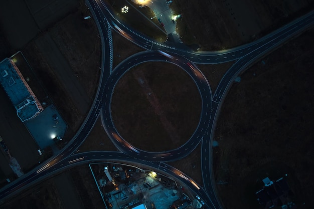Vista aérea da interseção da rotatória da estrada com tráfego pesado em movimento rápido à noite. Vista superior da encruzilhada de transporte circular urbano. Hora do rush com luzes de trilha de carro borradas.