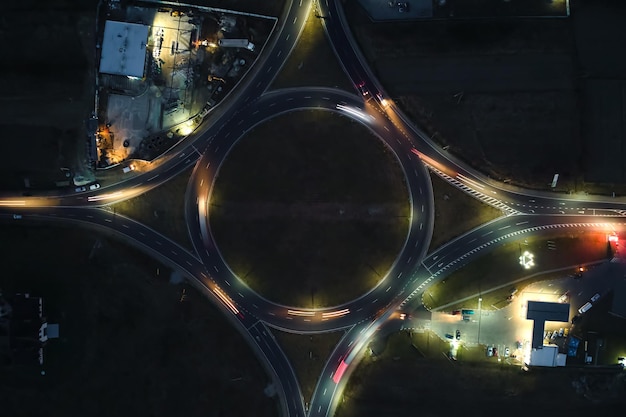 Vista aérea da interseção da rotatória da estrada com tráfego pesado em movimento rápido à noite. Vista superior da encruzilhada de transporte circular urbano. Hora do rush com luzes de trilha de carro borradas.