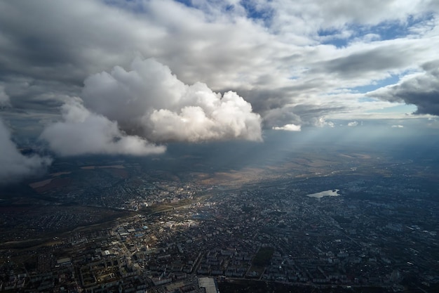 Vista aérea da janela do avião em alta altitude da cidade distante coberta de nuvens cumulus inchadas se formando antes da tempestade