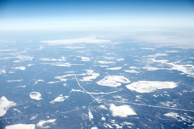 Vista aérea da janela do avião sobre nuvens no topo para campos e estradas de rios cobertos de neve