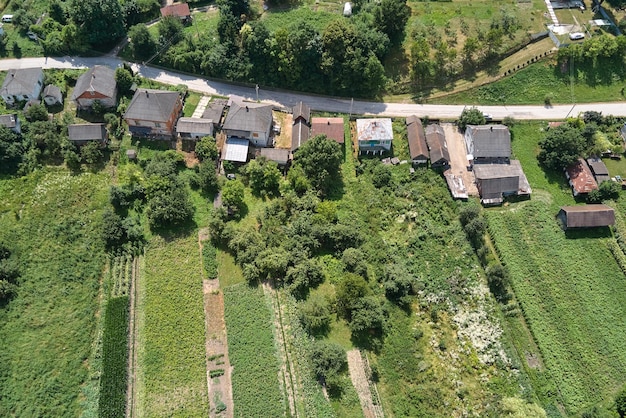 Vista aérea da paisagem de casas de aldeia e campos agrícolas cultivados verdes distantes com culturas em crescimento no dia de verão brilhante