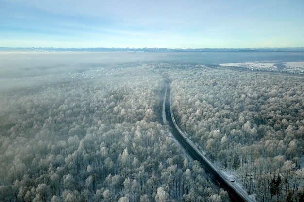 Vista aérea da paisagem de inverno com bosques cobertos de neve e estrada de floresta de asfalto preto em dia frio de inverno