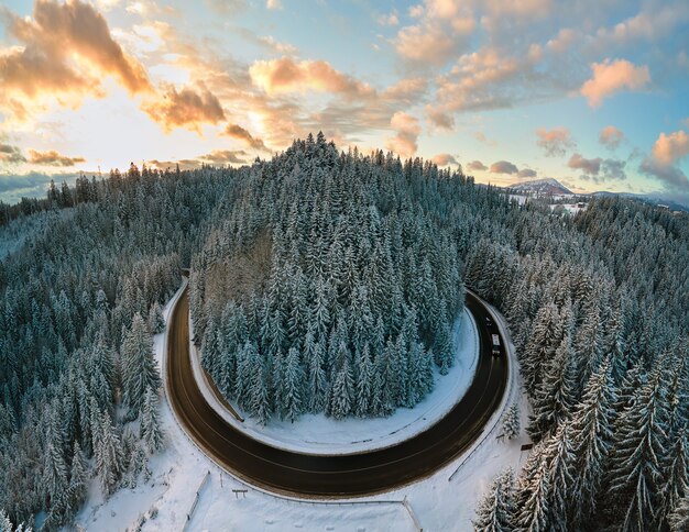 Vista aérea da paisagem de inverno com montanhas cobertas de neve e uma estrada florestal sinuosa na manhã.