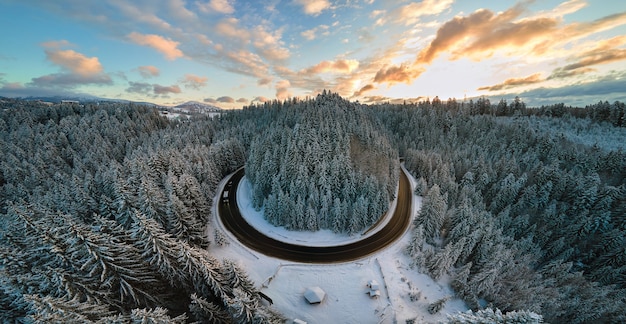 Vista aérea da paisagem de inverno com montanhas cobertas de neve e uma estrada florestal sinuosa na manhã.