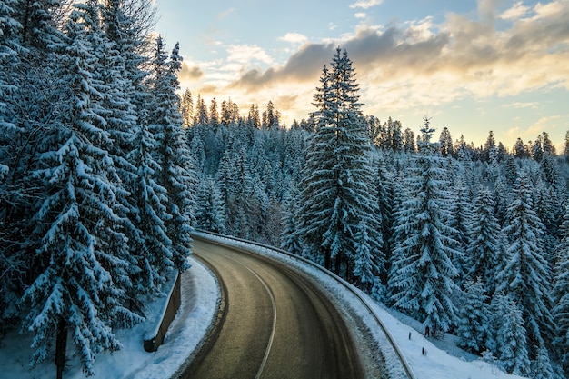 Vista aérea da paisagem de inverno com montanhas cobertas de neve e uma estrada florestal sinuosa na manhã.