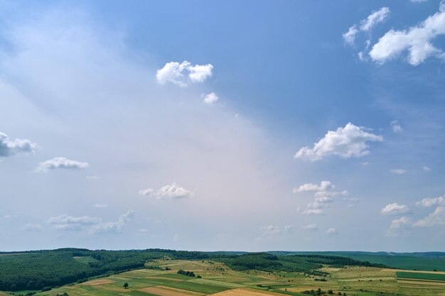 Vista aérea da paisagem do céu azul claro sobre campos agrícolas cultivados verdes com culturas em crescimento e florestas distantes no dia de verão brilhante