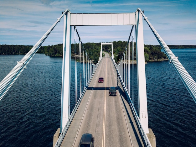 Vista aérea da ponte suspensa branca com carro atravessando o lago azul profundo no verão rural Finlândia
