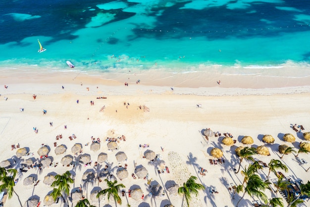 Vista aérea da praia tropical do Caribe com guarda-sóis de palha, palmeiras e barcos