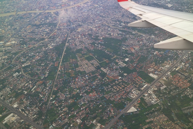 Vista aérea de Banguecoque, Tailândia com construção na cidade grande, no rio e na asa do avião.