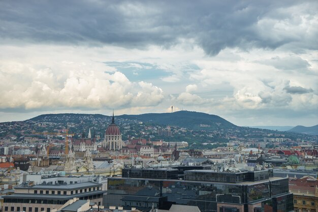 Vista aérea de Budapeste com colinas verdes e nuvens de chuva.