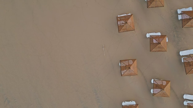 Vista aérea de cadeiras de sol e guarda-chuvas de palha na praia da manhã sem pessoas