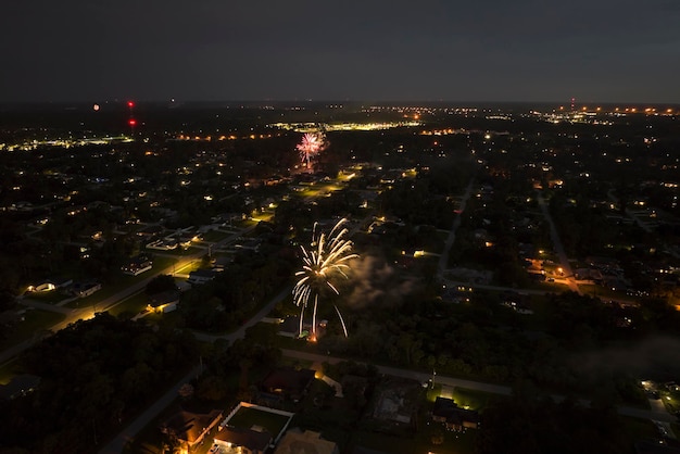 Vista aérea de fogos de artifício brilhantes explodindo com luzes coloridas sobre casas suburbanas em área residencial no feriado do Dia da Independência dos EUA