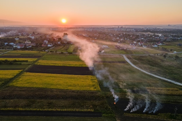 Vista aérea de fogueiras de resíduos agrícolas de capim seco e palha queimando com fumaça densa poluindo o ar durante a estação seca em fazendas, causando aquecimento global e gases cancerígenos