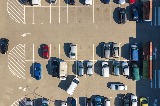 Vista aérea de muitos carros coloridos estacionados no estacionamento com linhas e marcações para lugares de estacionamento e direções.