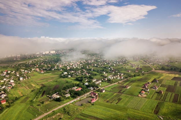 Vista aérea de nuvens brancas acima de uma cidade ou vila com fileiras de edifícios e ruas sinuosas entre campos verdes