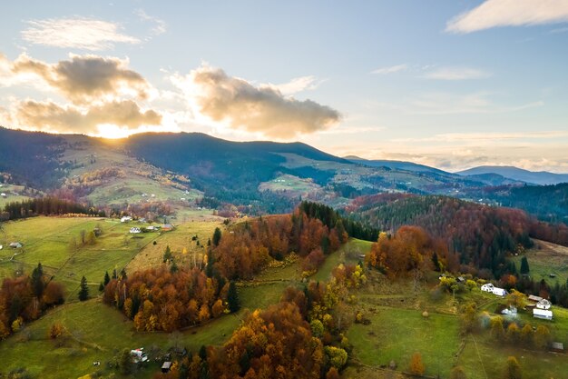 Vista aérea de pequenas casas de pastor em pastagens largas entre a floresta de outono nas montanhas dos Cárpatos ucranianos ao pôr do sol.