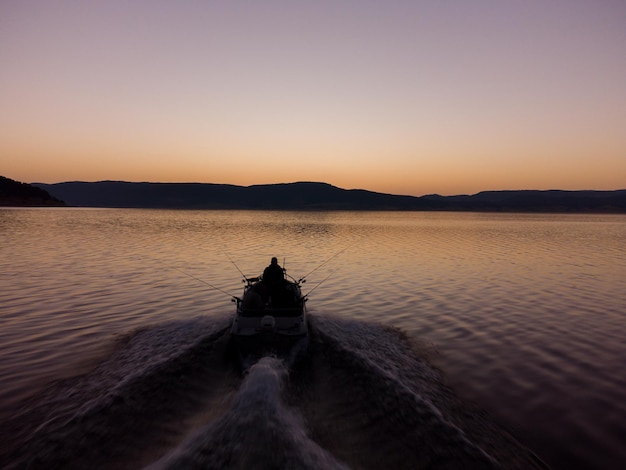 Vista aérea de pescadores em um barco a motor de velocidade pescando em um lago com belo nascer do sol