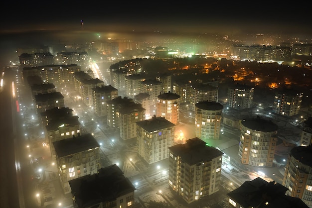 Vista aérea de prédios de apartamentos altos e ruas iluminadas brilhantes na área residencial da cidade à noite. Paisagem urbana escura