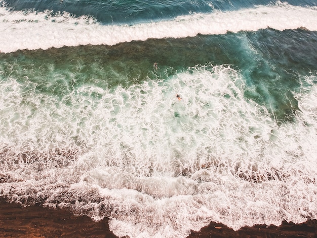 Vista aérea de surfistas nas ondas do Oceano Atlântico. Praia de areia