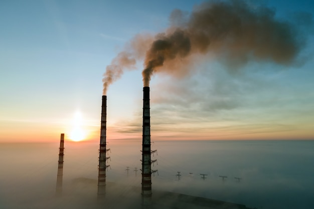 Vista aérea de tubos altos de usina de carvão com fumaça preta subindo a atmosfera poluente ao pôr do sol.