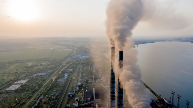 Vista aérea de tubos altos de usina de carvão com fumaça preta subindo a atmosfera poluente ao pôr do sol.