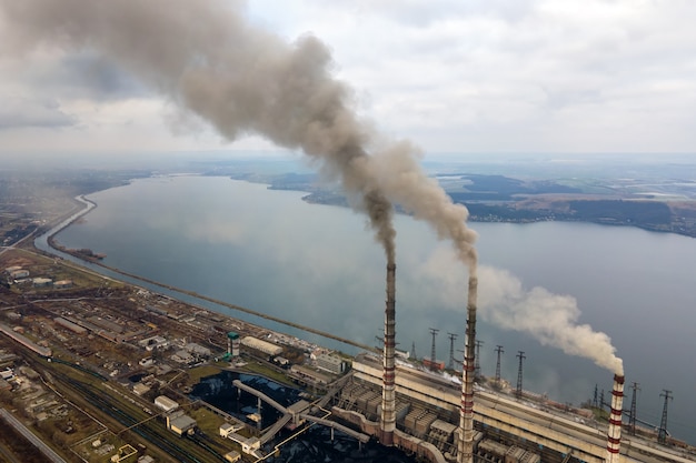 Vista aérea de tubos altos de usina de carvão com fumaça preta subindo a atmosfera poluente.