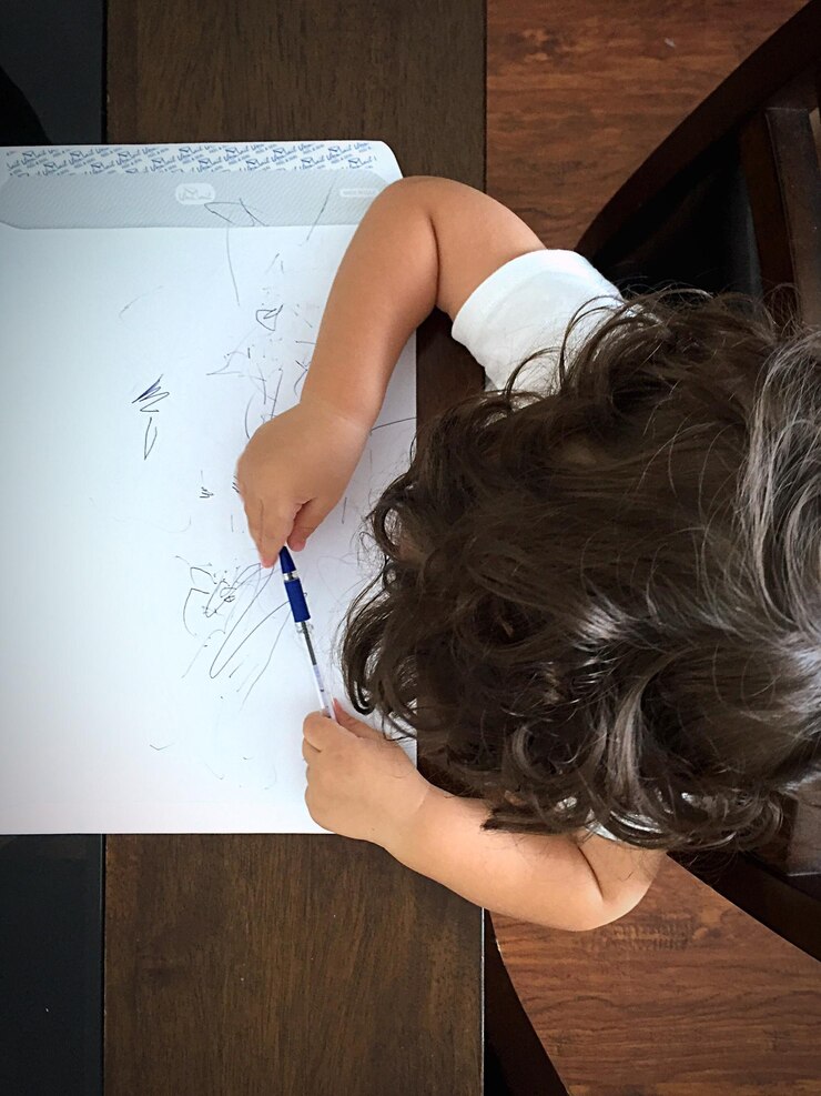 Foto vista aérea de um bebê rabiscando no papel na mesa