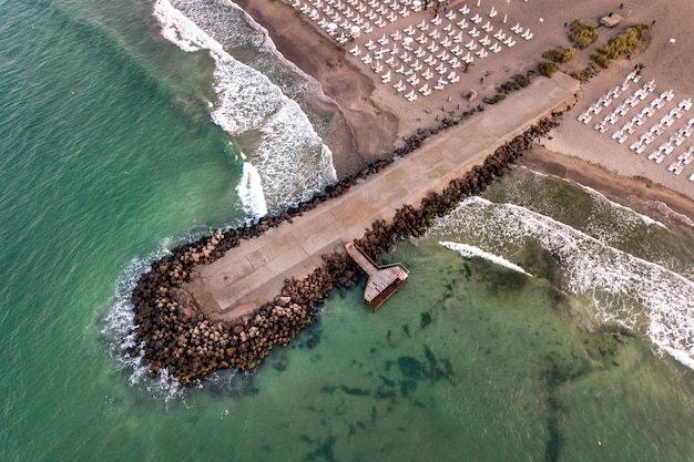 Vista aérea de um cais de concreto na beira-mar com ondas quebrando pedras.