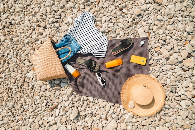 Vista aérea de um cobertor de praia com protetor solar e chapéu de palha creme com bolsa plana