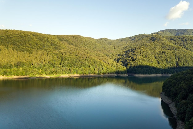 Vista aérea de um grande lago com águas azuis claras entre colinas de alta montanha cobertas por densa floresta perene
