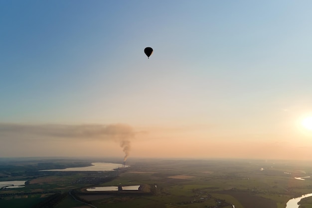 Vista aérea de um pequeno balão de ar quente sobrevoando a zona rural ao pôr do sol